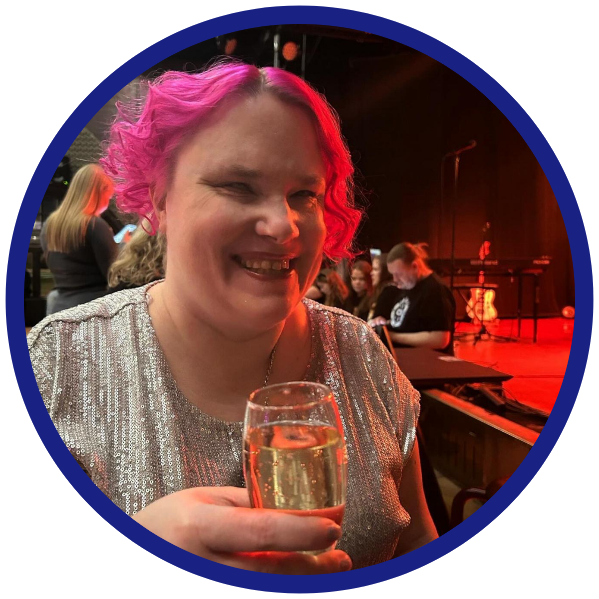 Valokuva Annukasta neonpinkissä kiharassa tukassa, hopeisessa paljettitopissa skumppalasi kädessä.