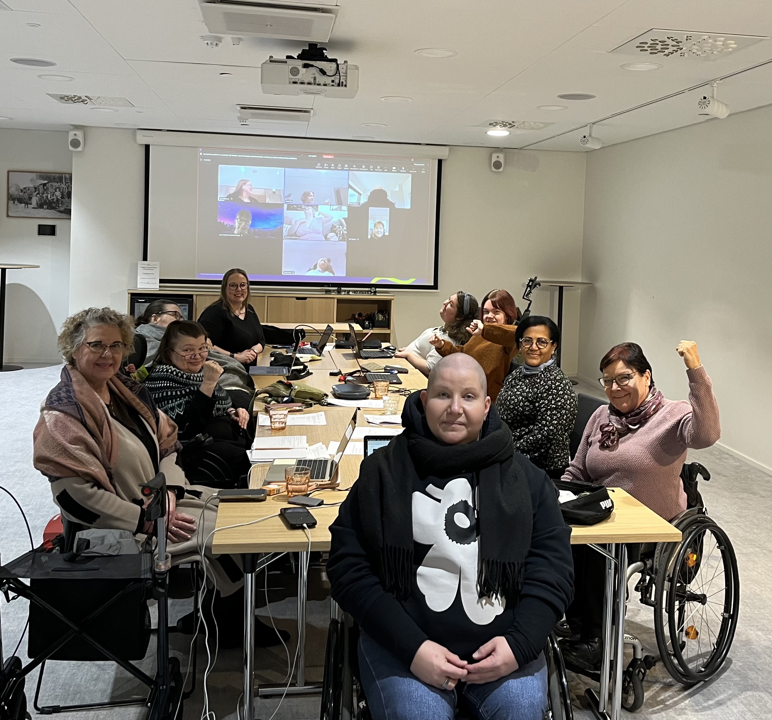 Valokuva kokoushuoneesta, jossa etualalla rusetin hallituksen jäsenet istuvat pöydään ääressä ja taka-alalla näkyy seinällä heijastettuna loput jäsenet teamsin välityksellä.